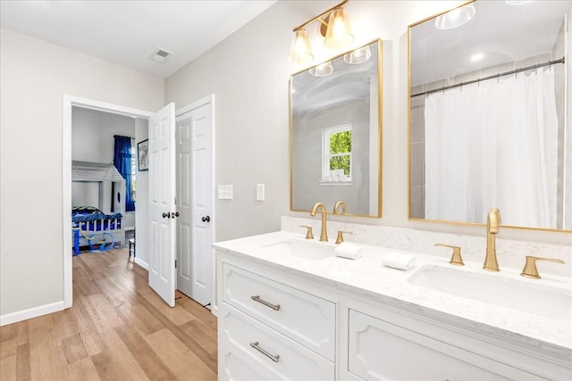 full bath with a sink, visible vents, double vanity, and wood finished floors