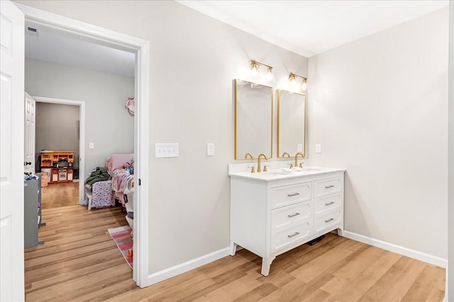 bathroom featuring wood finished floors, double vanity, a sink, and baseboards