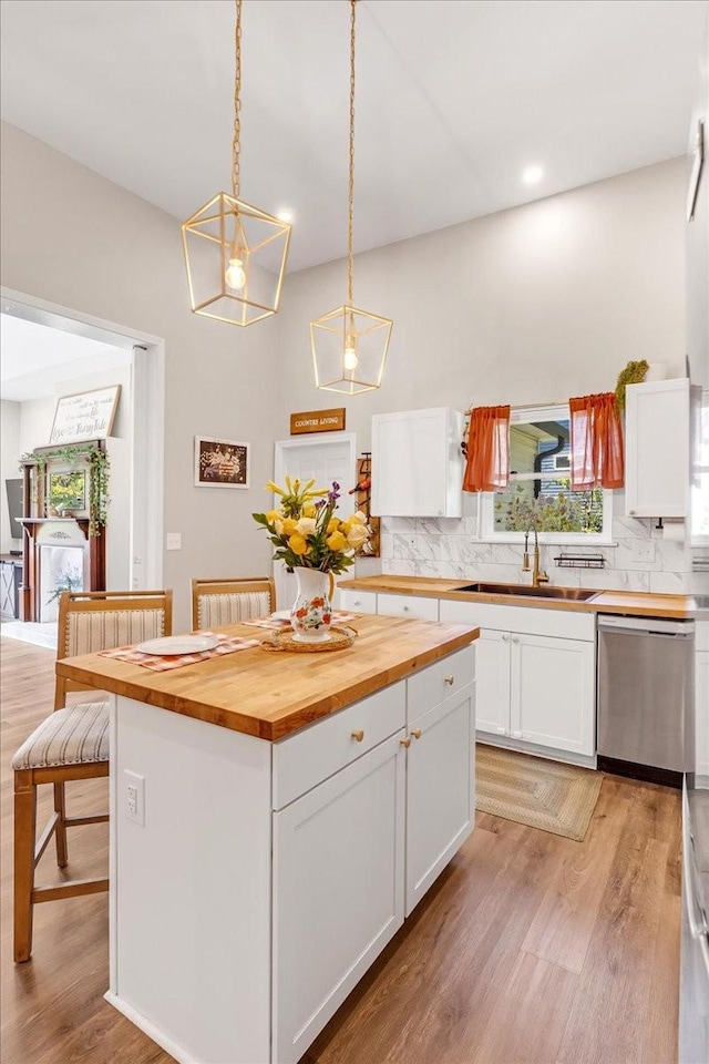 kitchen with white cabinetry, backsplash, wooden counters, stainless steel dishwasher, and a sink