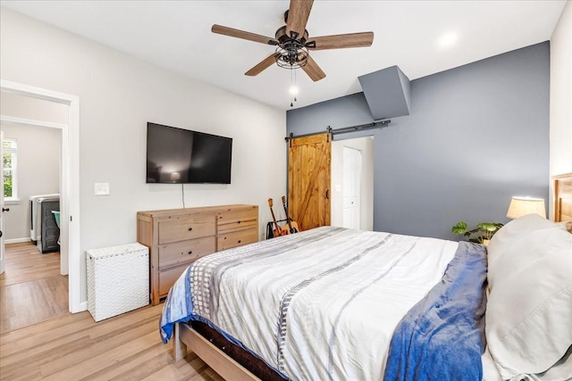 bedroom featuring a barn door, light wood-style floors, baseboards, and a ceiling fan