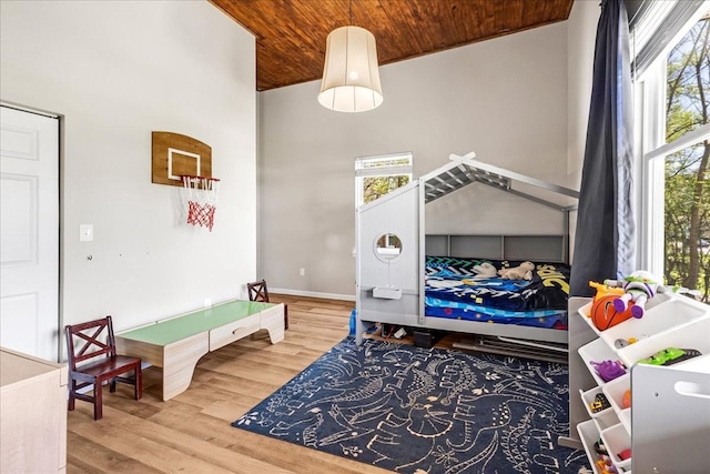 bedroom featuring wooden ceiling, wood finished floors, a towering ceiling, and multiple windows