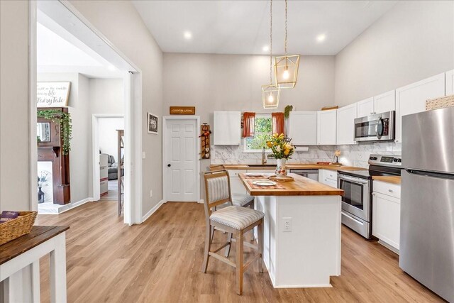 kitchen with tasteful backsplash, white cabinets, butcher block counters, a towering ceiling, and stainless steel appliances