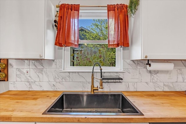 kitchen with white cabinets, butcher block countertops, a sink, and decorative backsplash