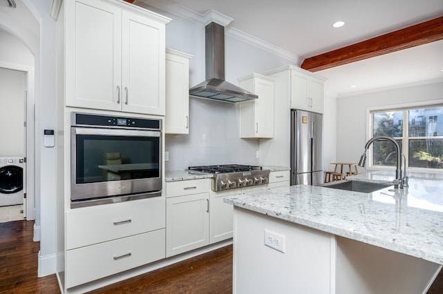 kitchen featuring crown molding, washer / clothes dryer, wall chimney exhaust hood, stainless steel appliances, and a sink