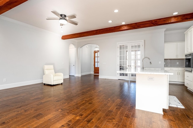 kitchen with dark wood-type flooring, decorative backsplash, a sink, arched walkways, and beam ceiling