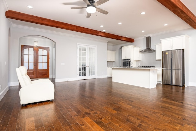 kitchen with beamed ceiling, appliances with stainless steel finishes, arched walkways, wall chimney range hood, and french doors