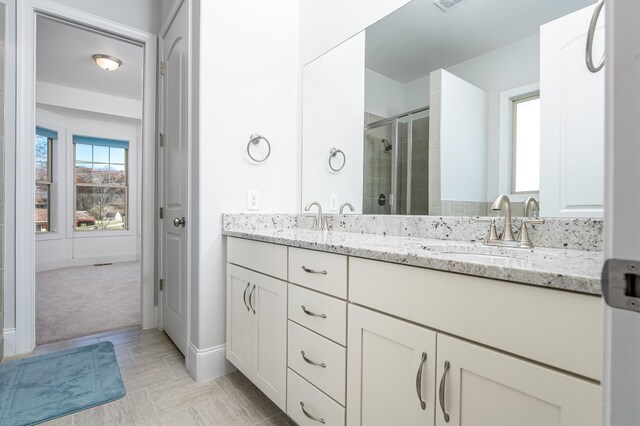 full bathroom with baseboards, double vanity, a sink, and a stall shower