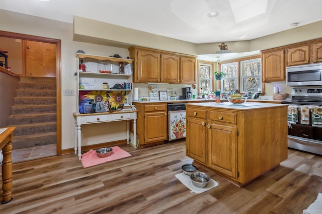kitchen featuring light countertops, a center island, appliances with stainless steel finishes, brown cabinetry, and wood finished floors