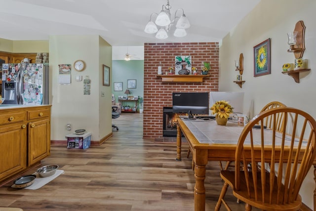 dining space with ceiling fan with notable chandelier, baseboards, a fireplace, and wood finished floors