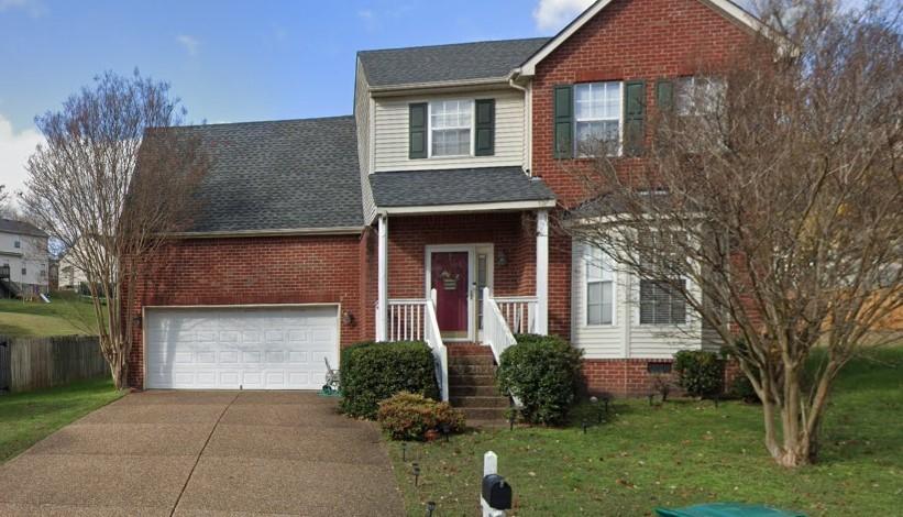 traditional home featuring concrete driveway, a front yard, brick siding, a garage, and a shingled roof
