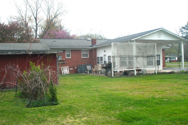 rear view of house with brick siding, a patio area, a lawn, and a chimney