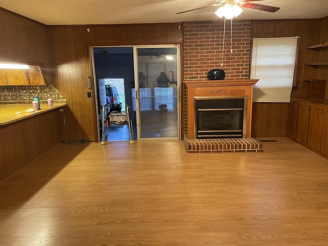 unfurnished living room featuring wood walls, a large fireplace, wood finished floors, and ceiling fan