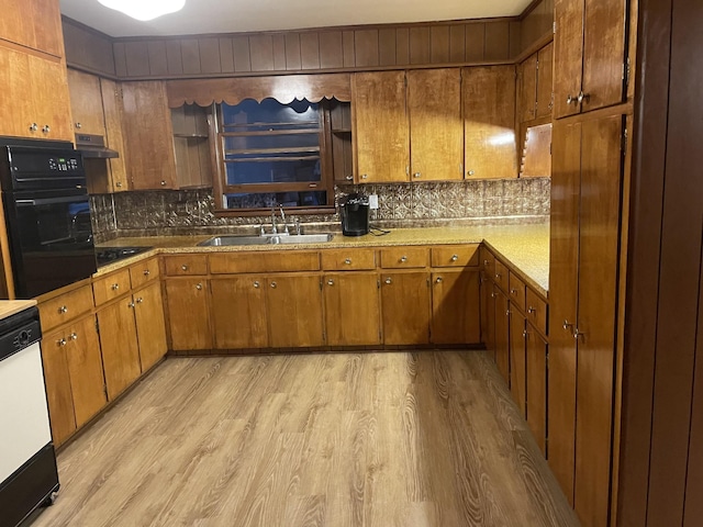 kitchen featuring light wood-style flooring, a sink, black appliances, and backsplash