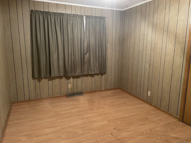 empty room with wooden walls, visible vents, and wood finished floors
