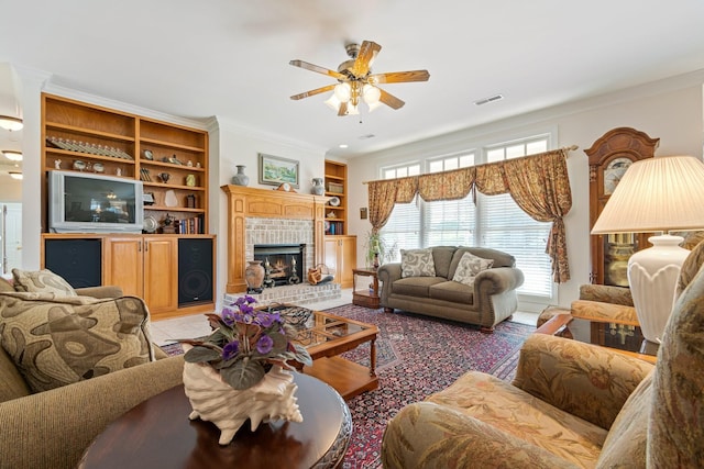 living room featuring visible vents, built in features, ceiling fan, a fireplace, and crown molding
