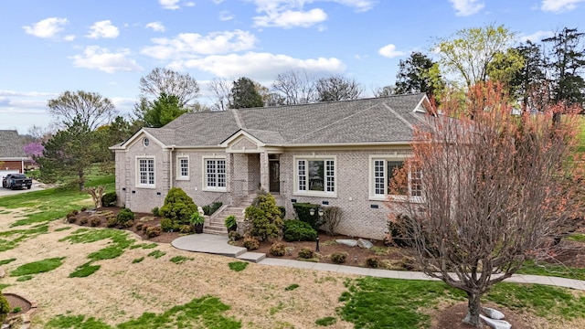 view of front facade with brick siding, a front lawn, and a shingled roof
