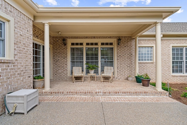 doorway to property featuring roof with shingles, a porch, and brick siding