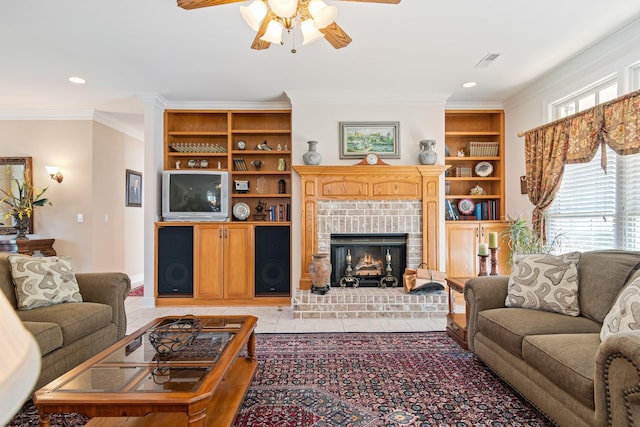 living area with light tile patterned floors, ornamental molding, a ceiling fan, a brick fireplace, and built in shelves