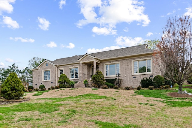 view of front of home featuring roof with shingles, a front yard, and brick siding