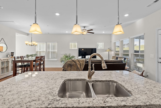 kitchen featuring open floor plan, light stone countertops, visible vents, a sink, and hanging light fixtures