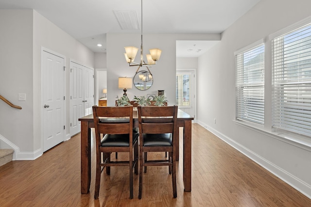 dining area featuring wood finished floors, an inviting chandelier, baseboards, and stairway