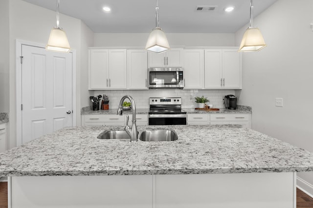 kitchen with white cabinets, appliances with stainless steel finishes, a sink, a center island with sink, and decorative backsplash