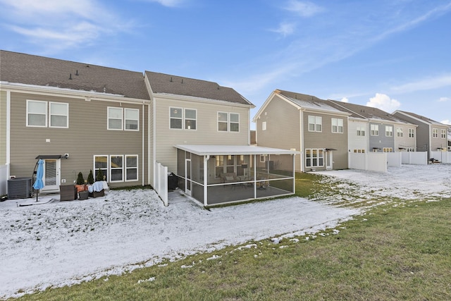 snow covered back of property with central AC, fence, and a sunroom