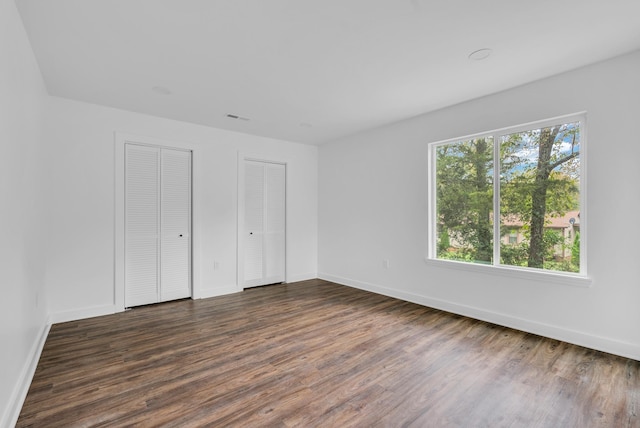 unfurnished bedroom featuring dark wood-style floors, baseboards, multiple closets, and visible vents