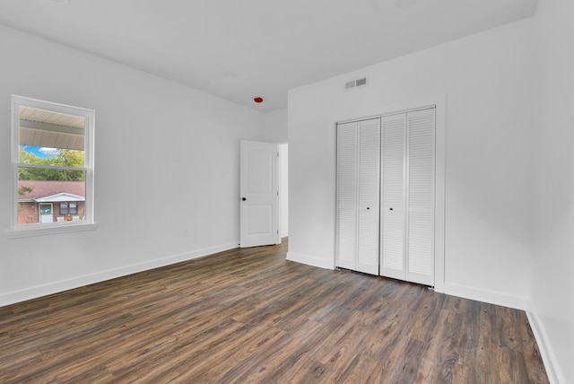 unfurnished bedroom featuring dark wood-style flooring, visible vents, baseboards, and a closet