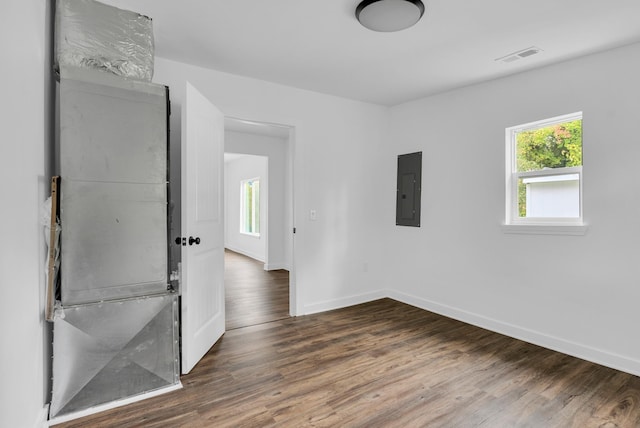 unfurnished room with electric panel, a healthy amount of sunlight, baseboards, and wood finished floors