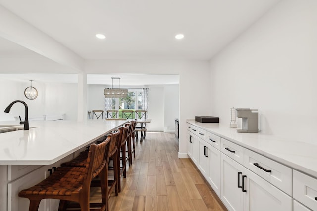 1048 Edgewater Cir, Gallatin, TN 37066 - kitchen with light wood-style flooring, a chandelier, decorative light fixtures, white cabinets, and a kitchen bar
