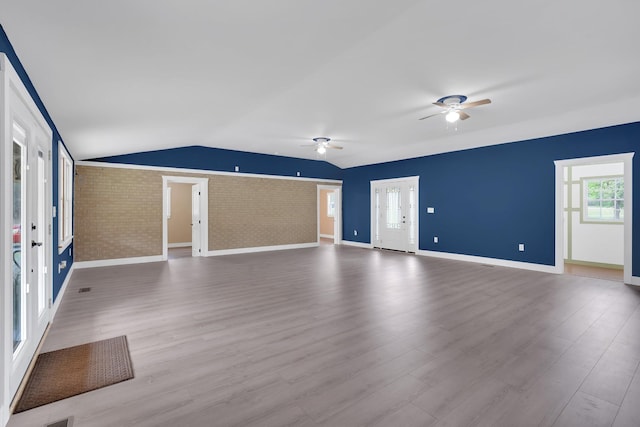unfurnished living room with brick wall, vaulted ceiling, a ceiling fan, and wood finished floors