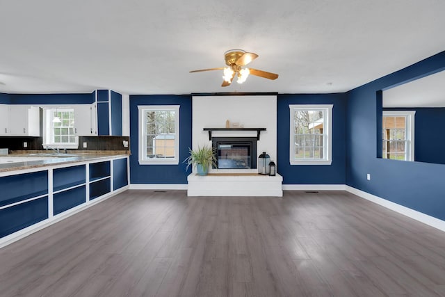 unfurnished living room featuring ceiling fan, a glass covered fireplace, a sink, baseboards, and dark wood-style floors