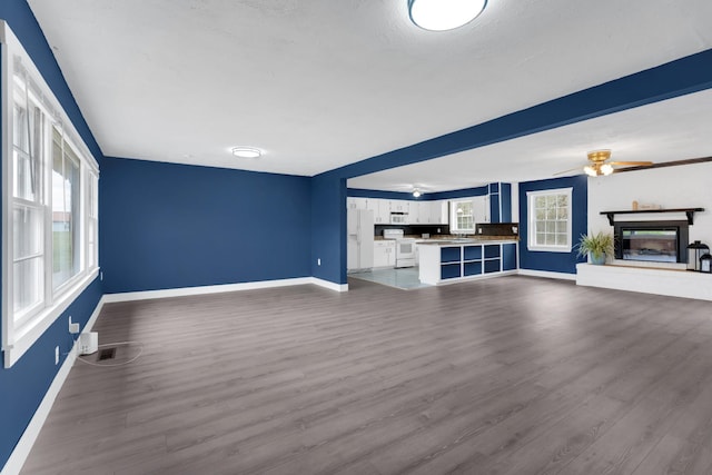 unfurnished living room with dark wood-type flooring, baseboards, a ceiling fan, and a glass covered fireplace