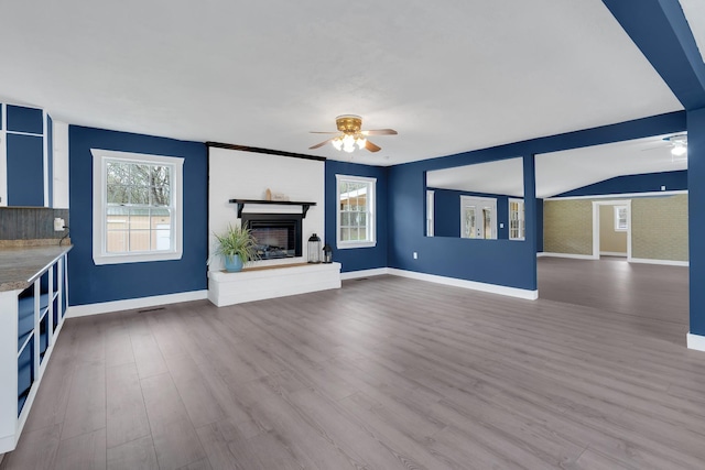 unfurnished living room with a healthy amount of sunlight, ceiling fan, a fireplace with raised hearth, and wood finished floors