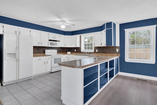 kitchen featuring white appliances, a peninsula, white cabinetry, a ceiling fan, and a sink