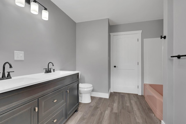 bathroom with toilet, a bath, wood finished floors, and a sink