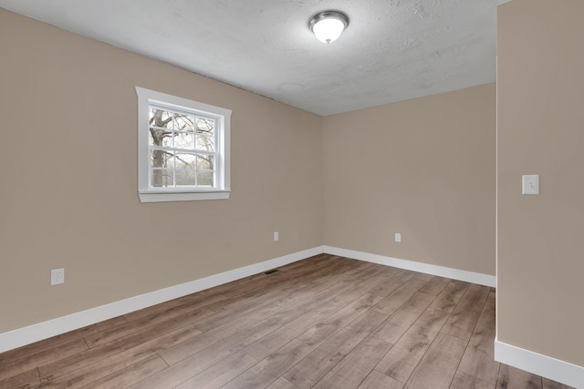 unfurnished room featuring a textured ceiling, wood finished floors, baseboards, and visible vents