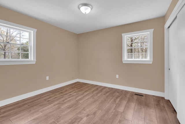 empty room with a wealth of natural light, visible vents, baseboards, and wood finished floors