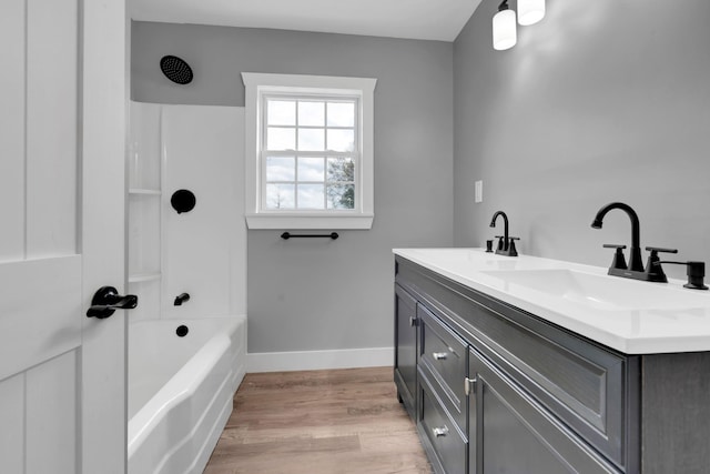 full bathroom with wood finished floors, double vanity, a sink, and baseboards