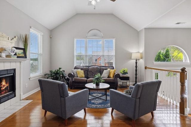 living area with baseboards, a tiled fireplace, ceiling fan, wood finished floors, and lofted ceiling