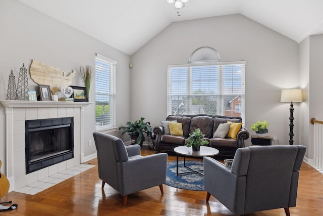 living room with light wood-style flooring, a tiled fireplace, a ceiling fan, and lofted ceiling