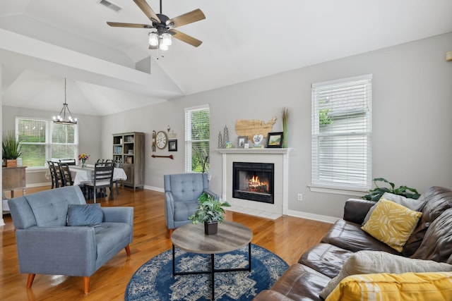 living room featuring a tiled fireplace, visible vents, light wood-style flooring, and ceiling fan with notable chandelier