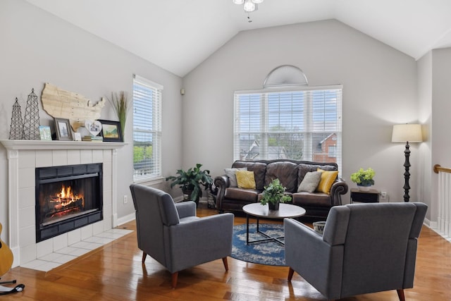 living area featuring light wood-style flooring, a tiled fireplace, a ceiling fan, and vaulted ceiling