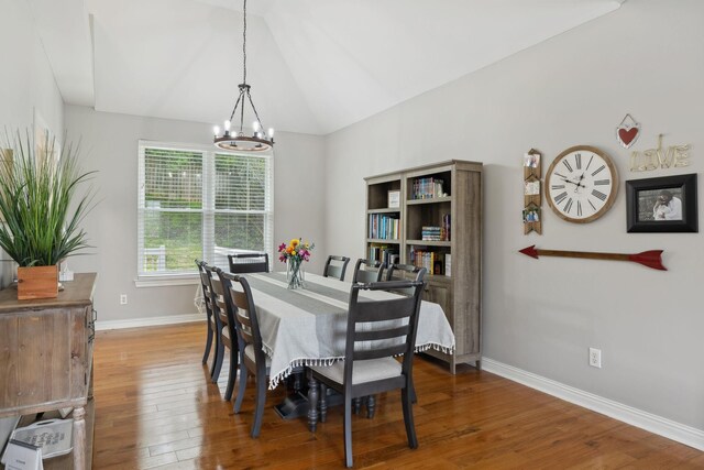 dining area featuring baseboards, hardwood / wood-style floors, a notable chandelier, and vaulted ceiling