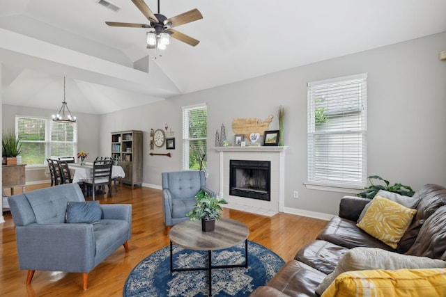 living area featuring wood finished floors, ceiling fan with notable chandelier, a tiled fireplace, and visible vents