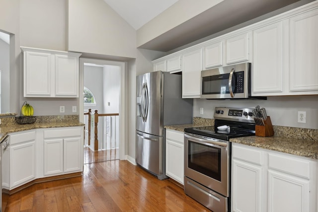 kitchen featuring stone counters, light wood-type flooring, vaulted ceiling, white cabinets, and appliances with stainless steel finishes