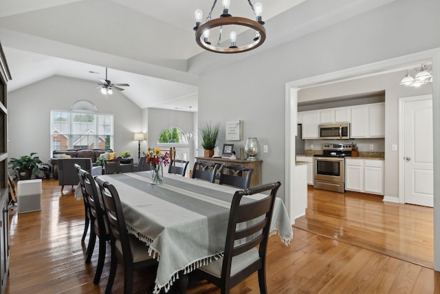 dining room with light wood-type flooring, ceiling fan with notable chandelier, and vaulted ceiling