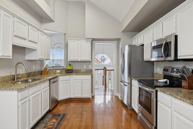 kitchen featuring white cabinetry, vaulted ceiling, wood finished floors, a sink, and stainless steel appliances