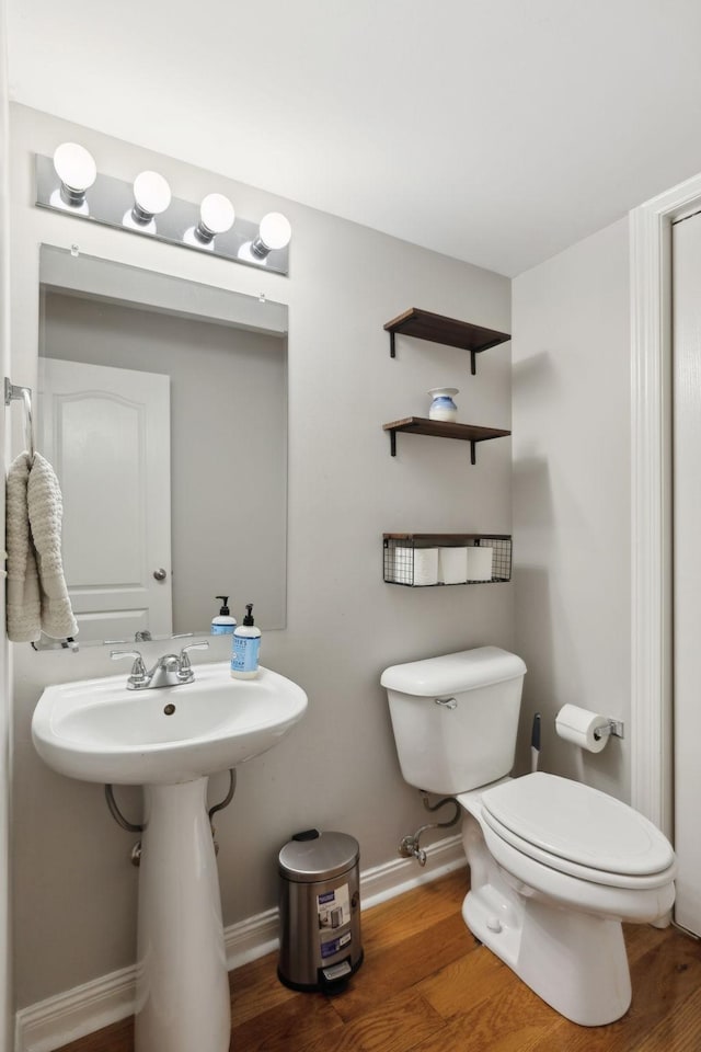 half bath with toilet, wood finished floors, and baseboards